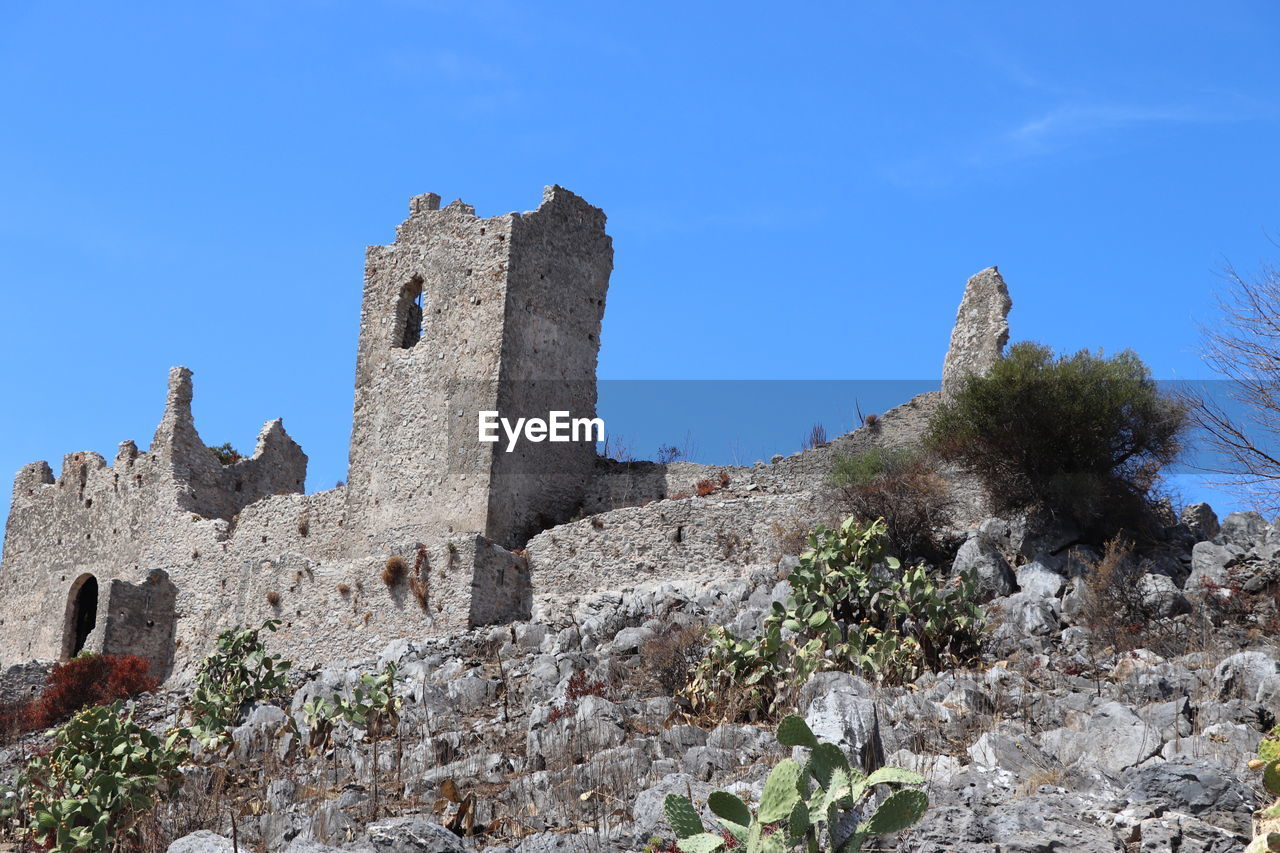 history, architecture, the past, sky, built structure, building, ruins, travel destinations, nature, castle, building exterior, blue, ancient, old ruin, travel, old, plant, fort, clear sky, no people, wall, tourism, stone material, tree, medieval, historic site, land, outdoors, low angle view, ruined, day, sunny, rock, ancient history, tower, fortification, religion, fortified wall, landscape, stone wall