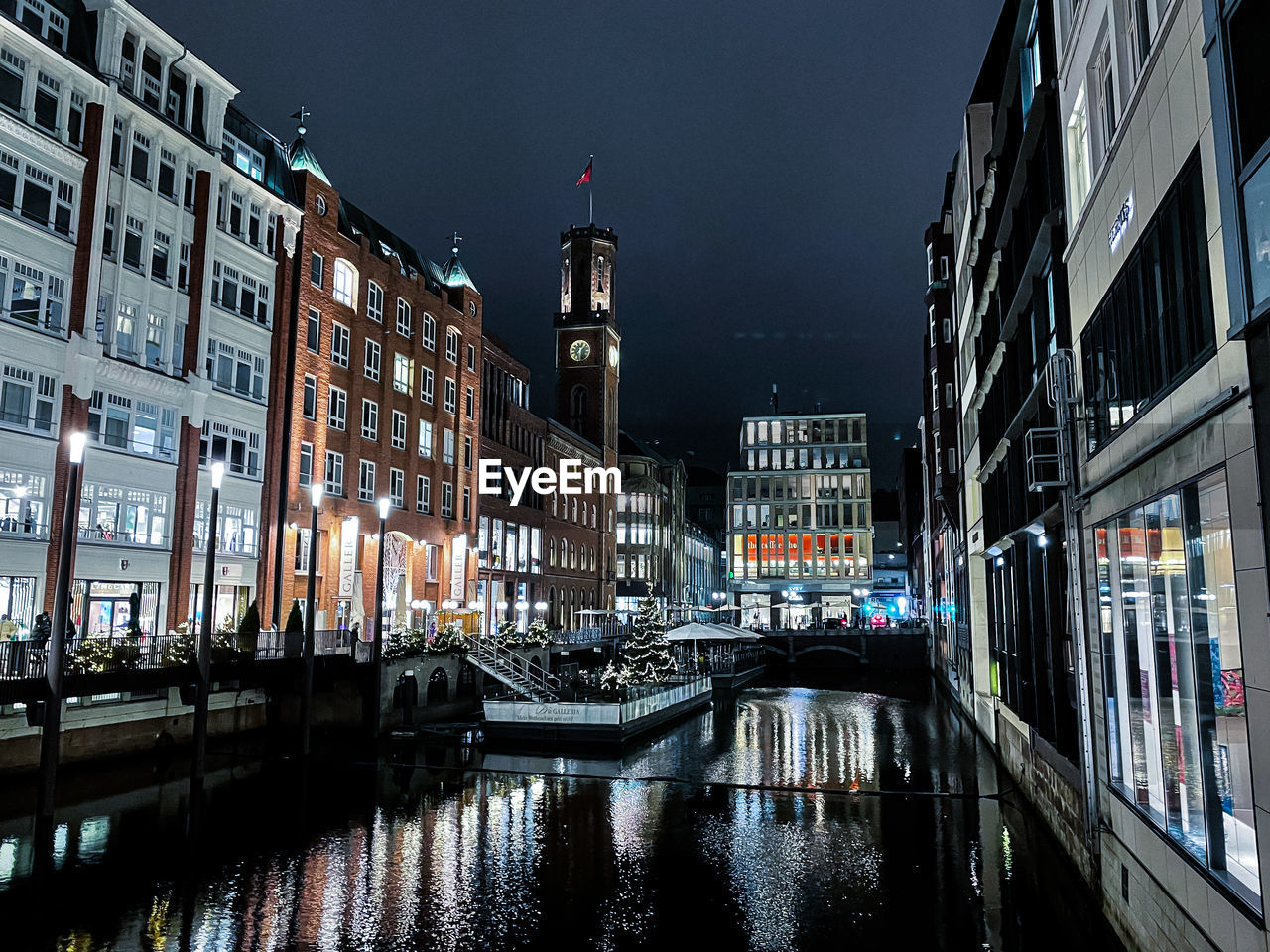 Canal by illuminated buildings in hamburg city at night