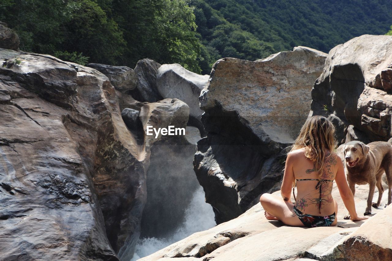 Rear view of woman sitting with dog on cliff