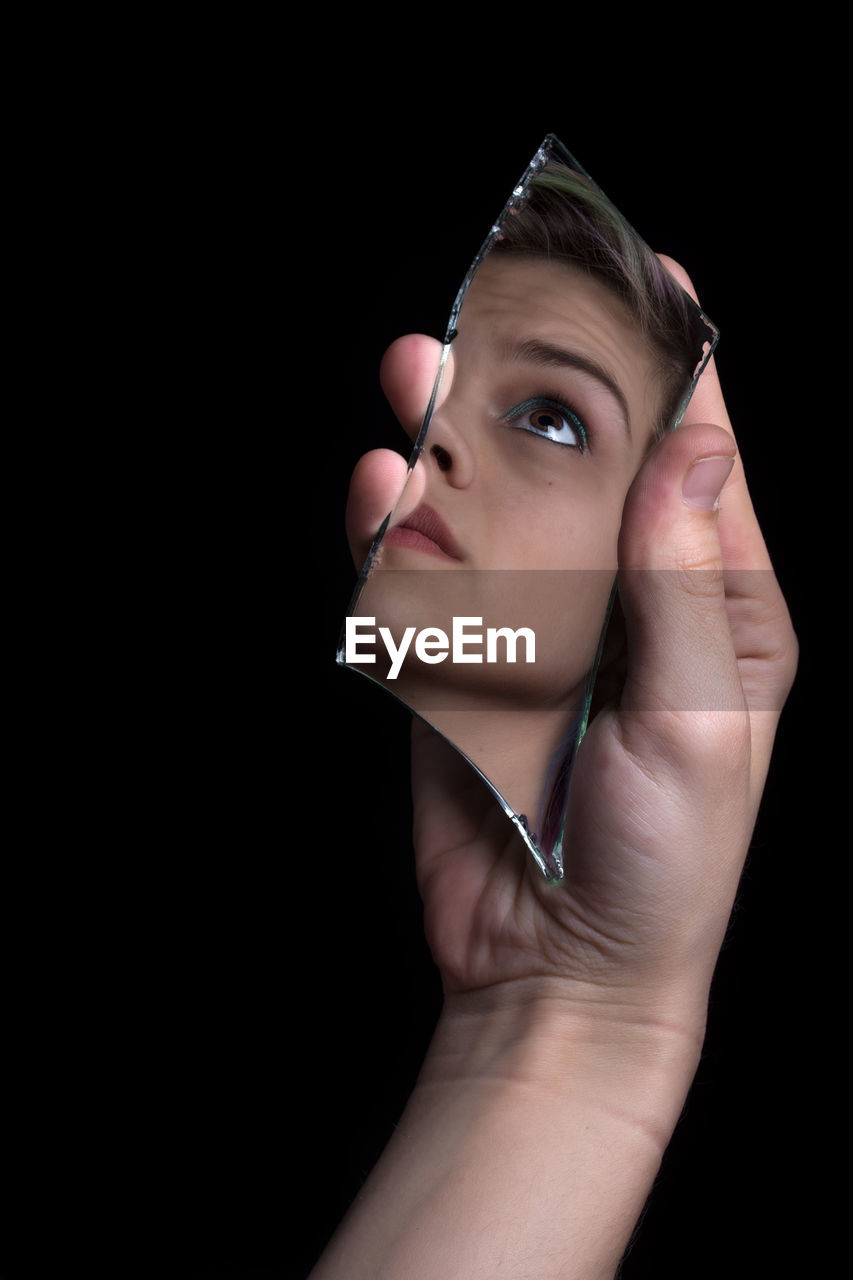 Cropped hand of young woman reflecting on mirror against black background