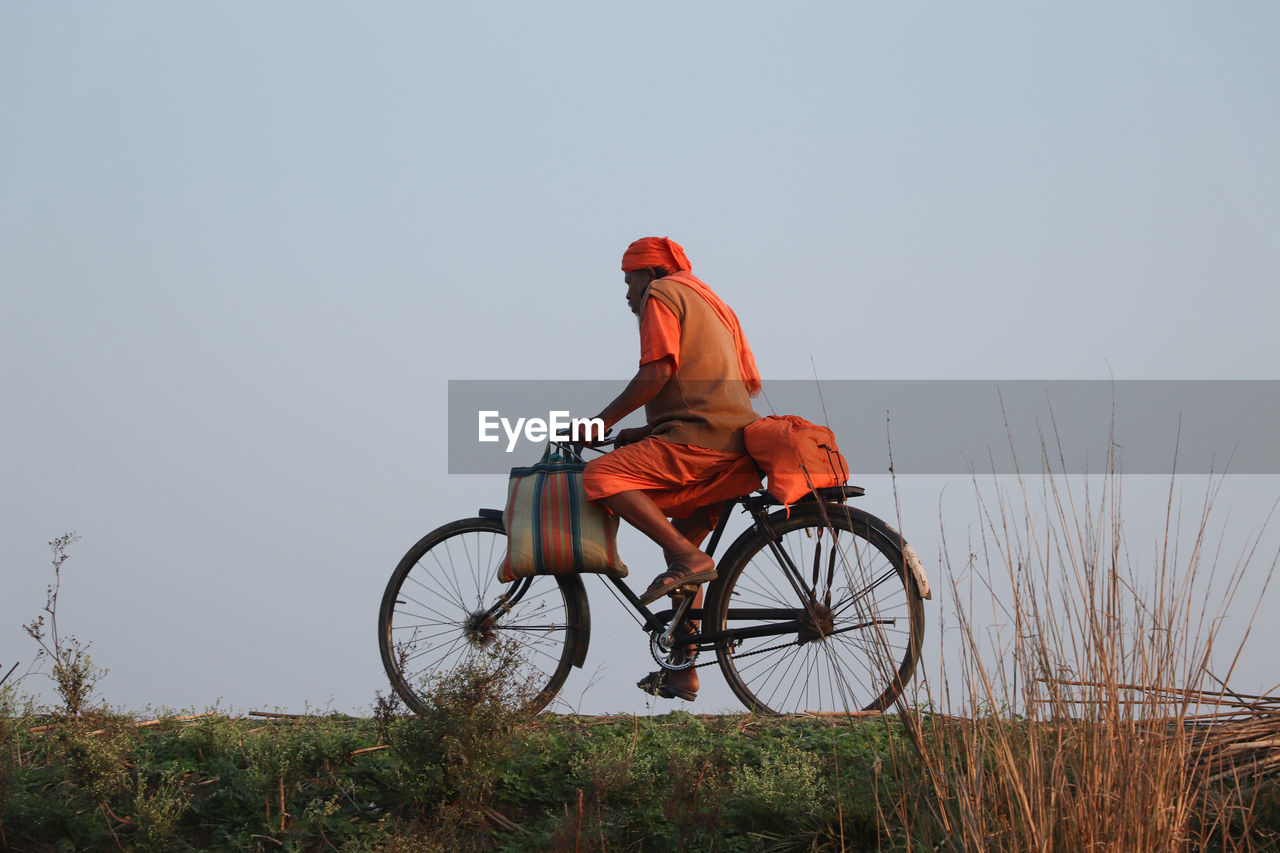 MAN RIDING BICYCLE ON GRASSY FIELD AGAINST SKY