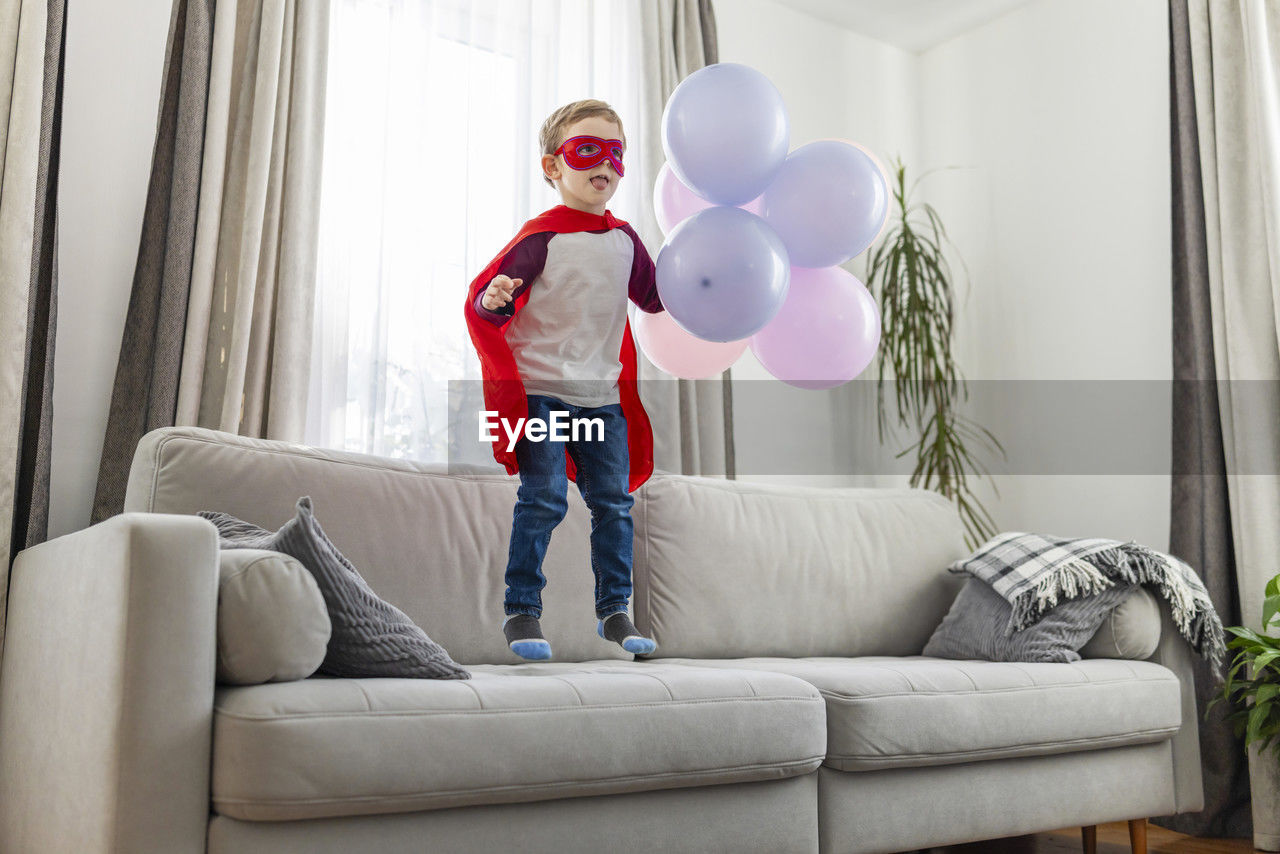 full length of young woman with balloons while sitting on sofa at home