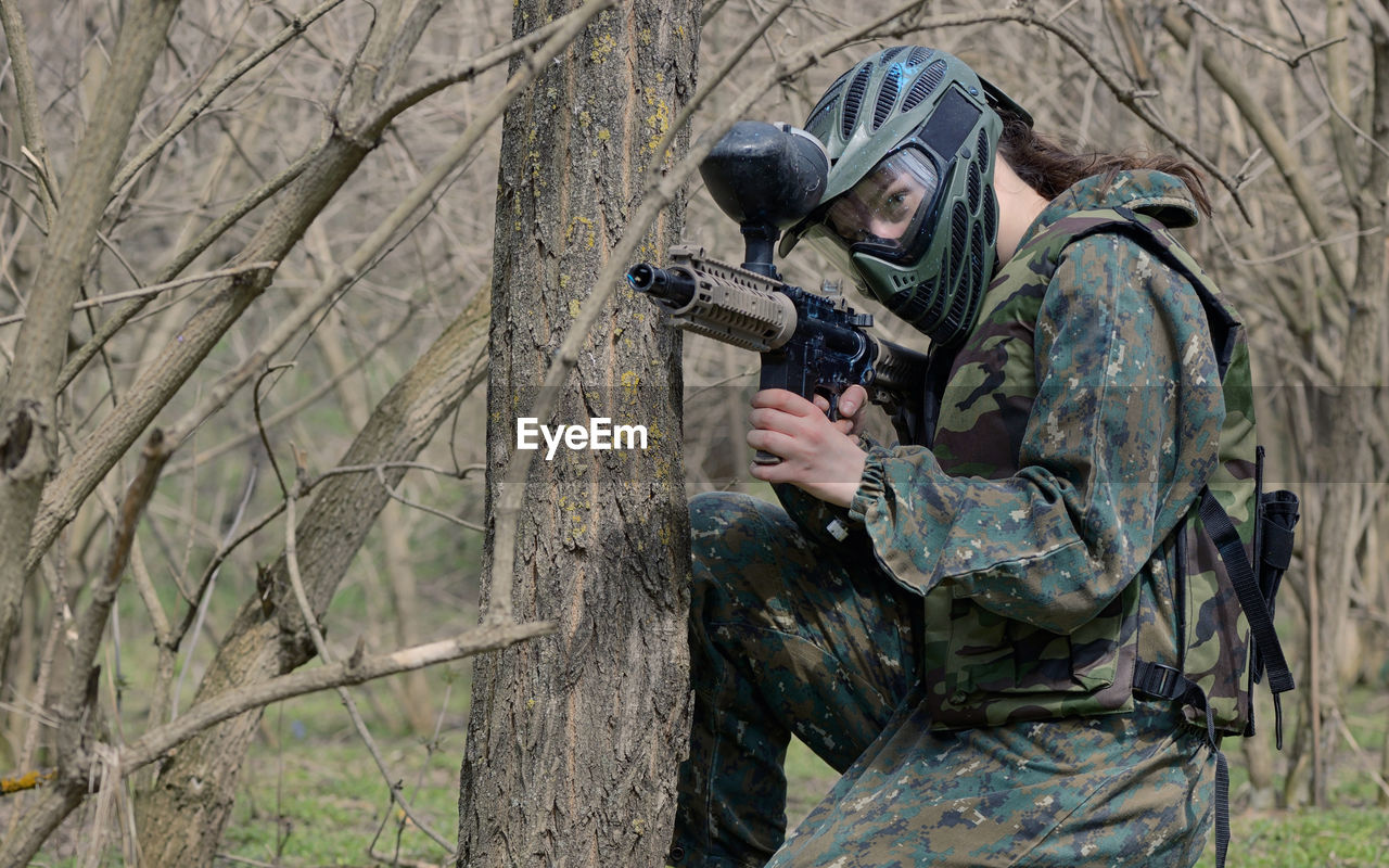 Army soldier aiming while kneeling amidst trees in forest