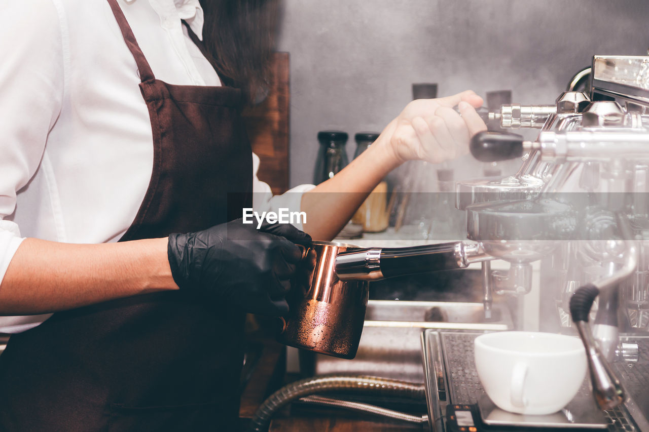 Midsection of woman making coffee at cafeteria