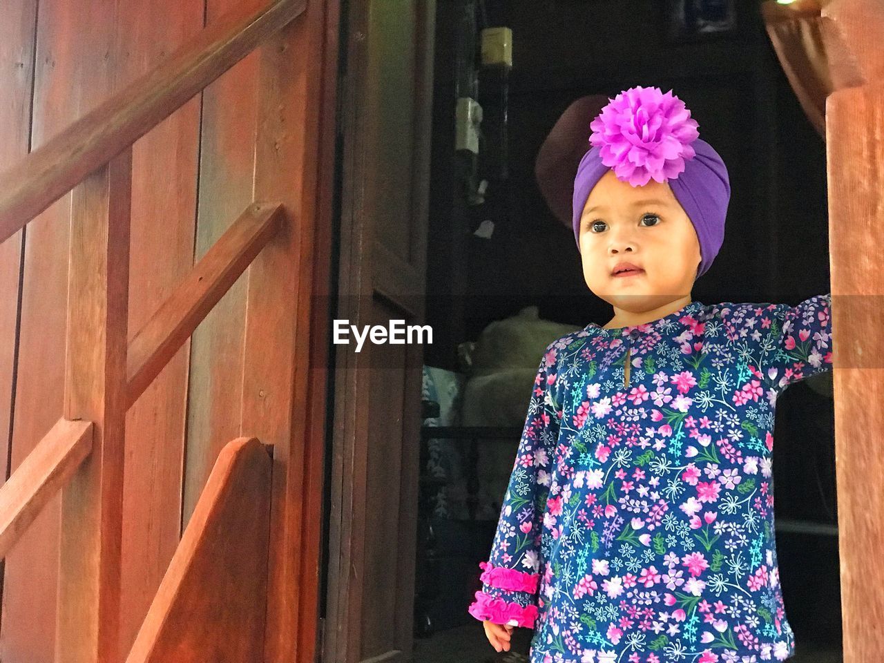 Cute baby girl wearing turban looking away while standing at doorway