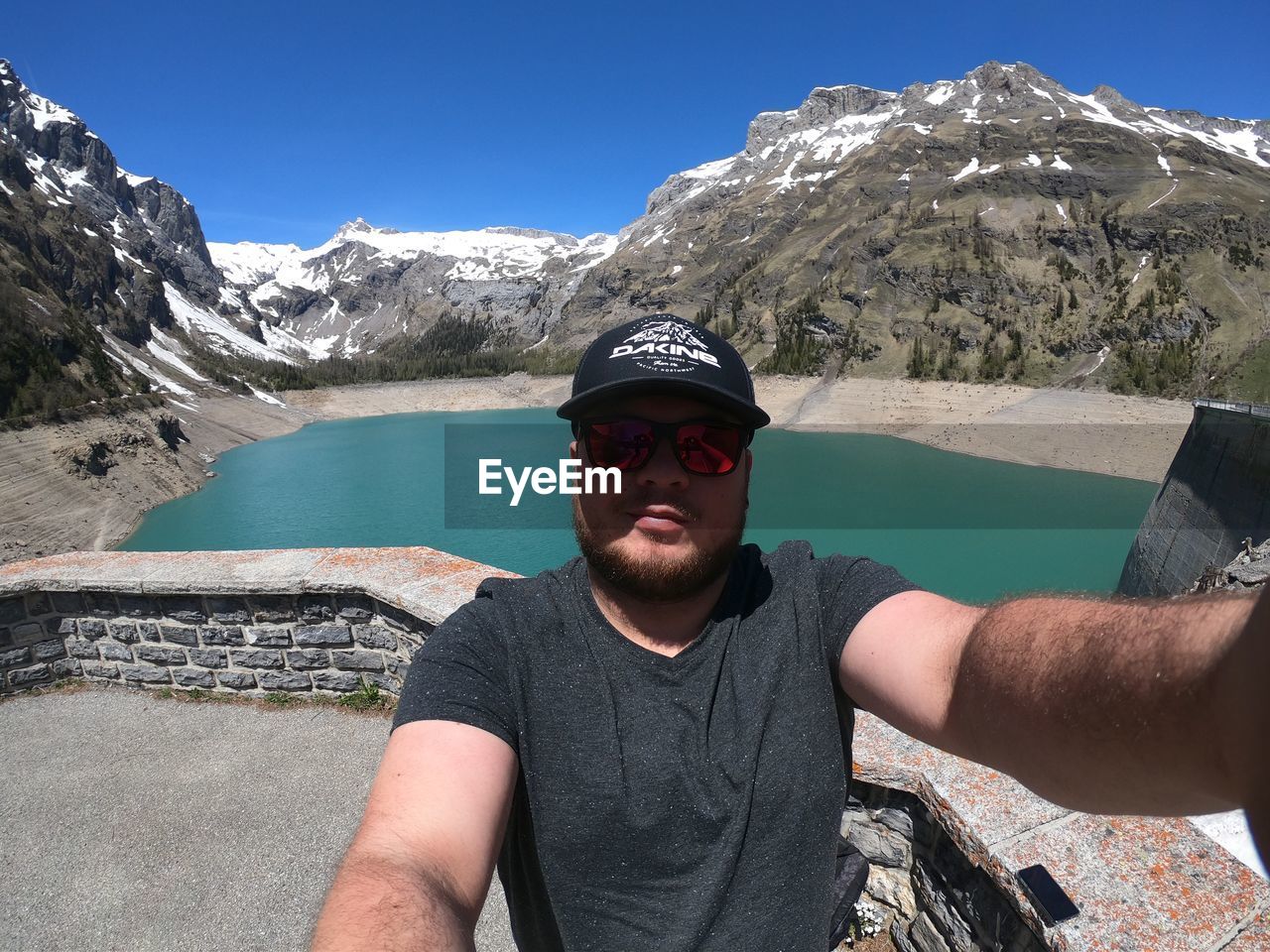 Portrait of young man in sunglasses against lake and mountains