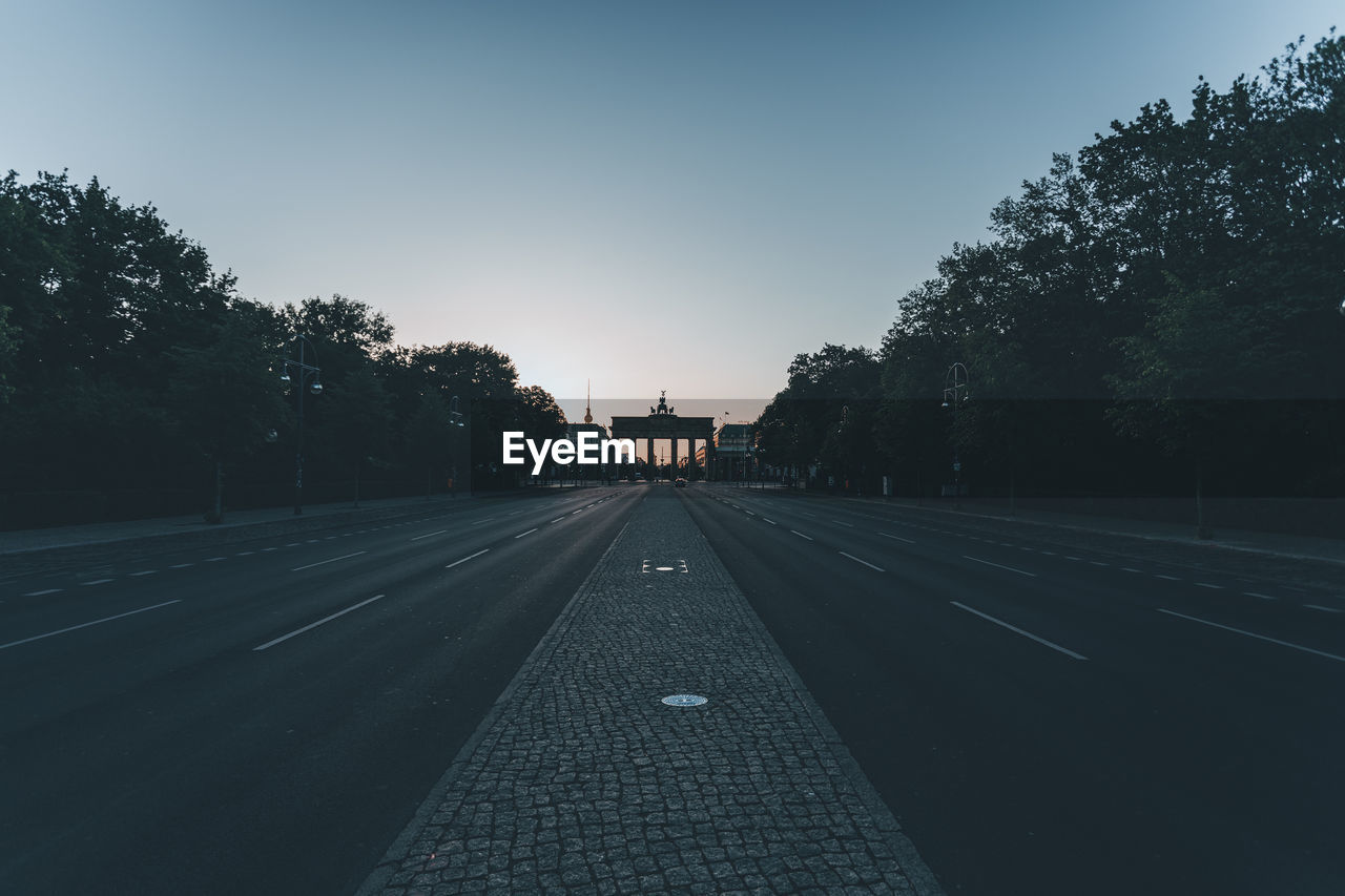 Empty road along trees and against sky