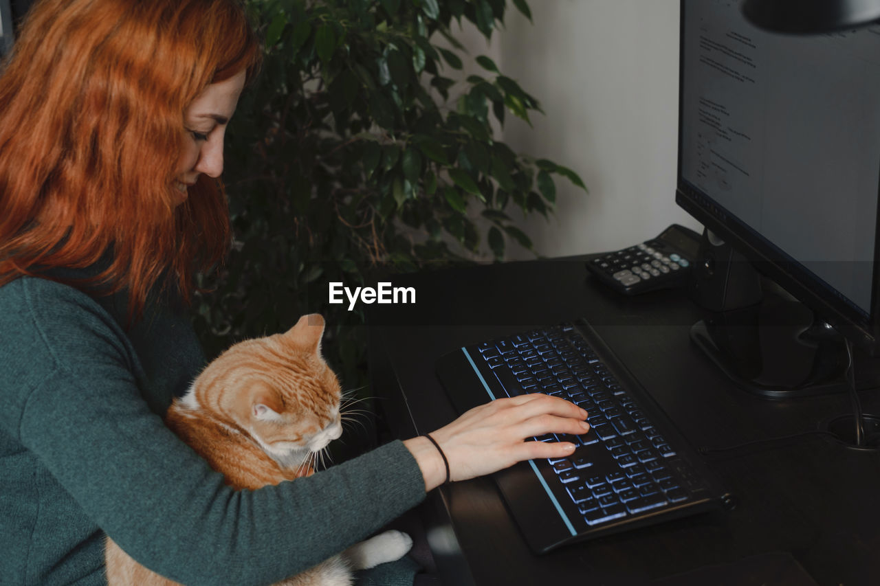 Woman working on keyboard and computer with cat on her laps. freelancer doing her work at home with