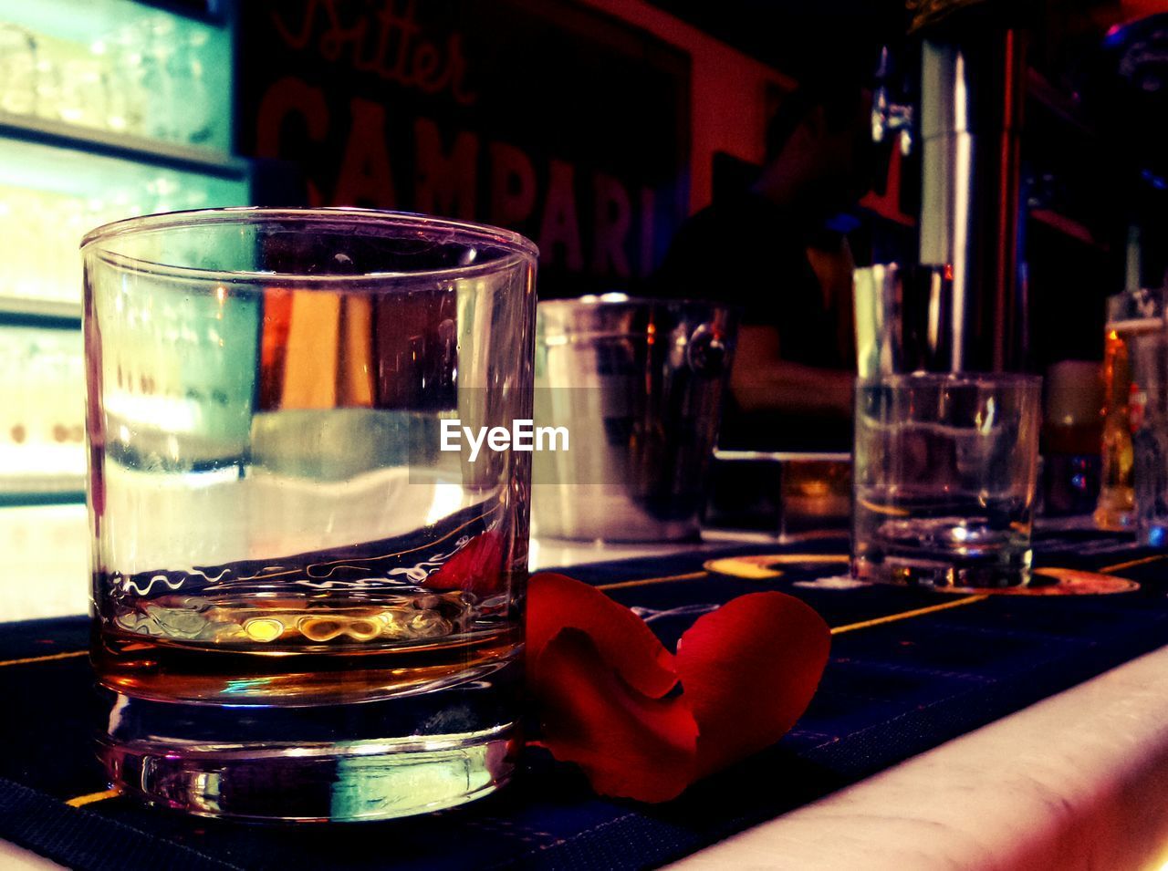 Close-up of scotch whisky in glass with red rose petal on bar counter at nightclub
