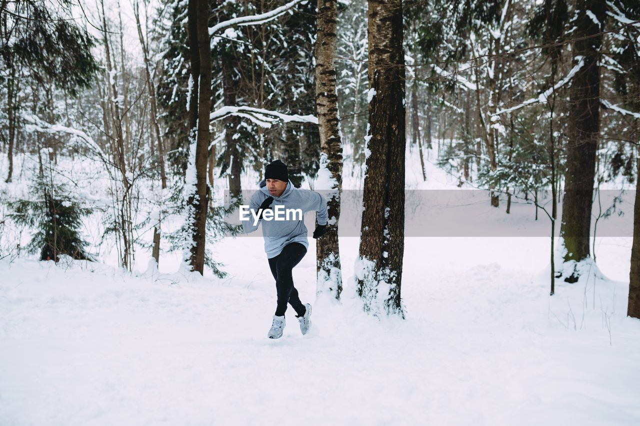 Full length of man running on snow covered field against trees