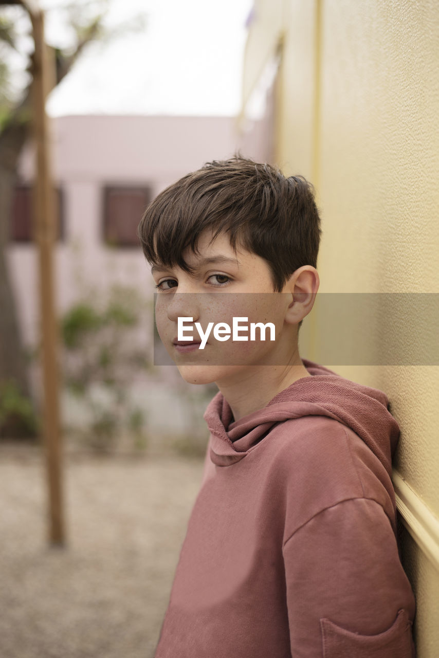 Portrait of a teenage boy leaning against wall looking camera