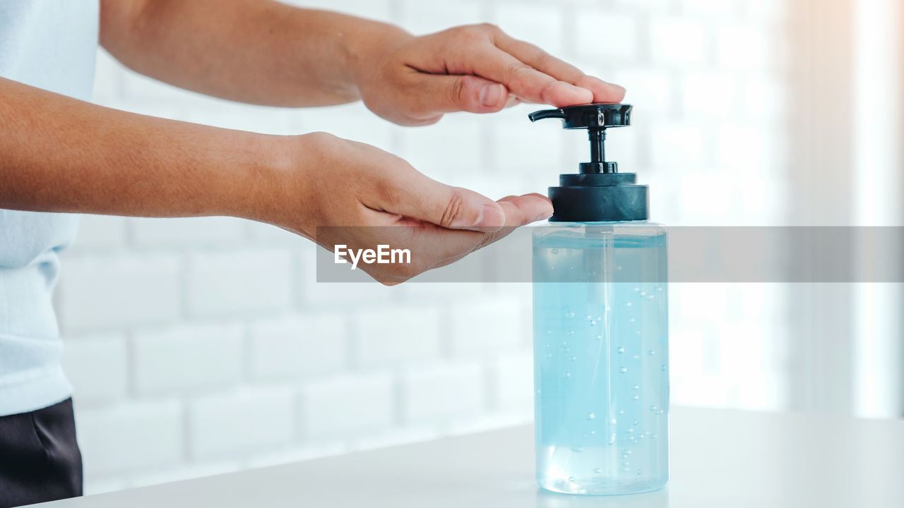 CLOSE-UP OF HAND HOLDING GLASS BOTTLE WITH OPEN