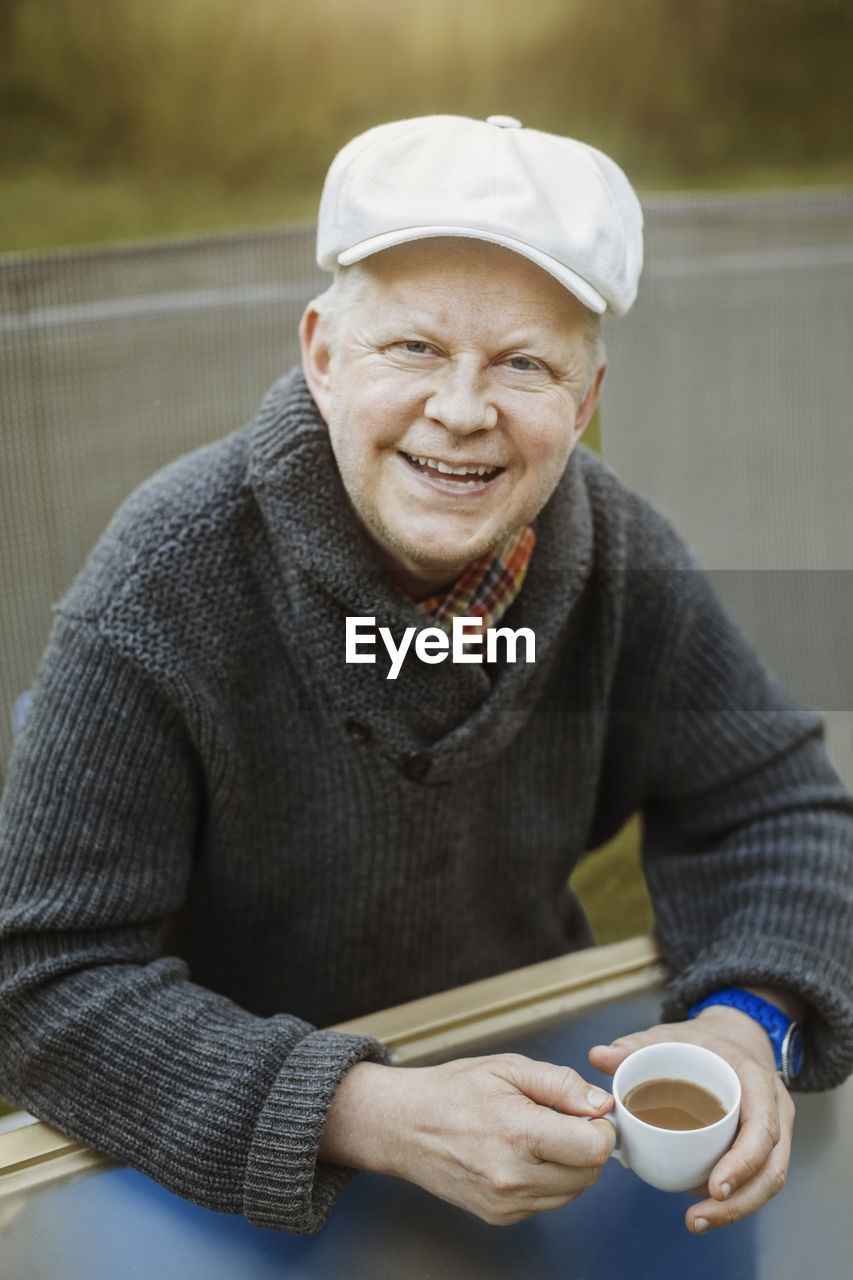 Portrait of happy man holding coffee cup while sitting at table outdoors