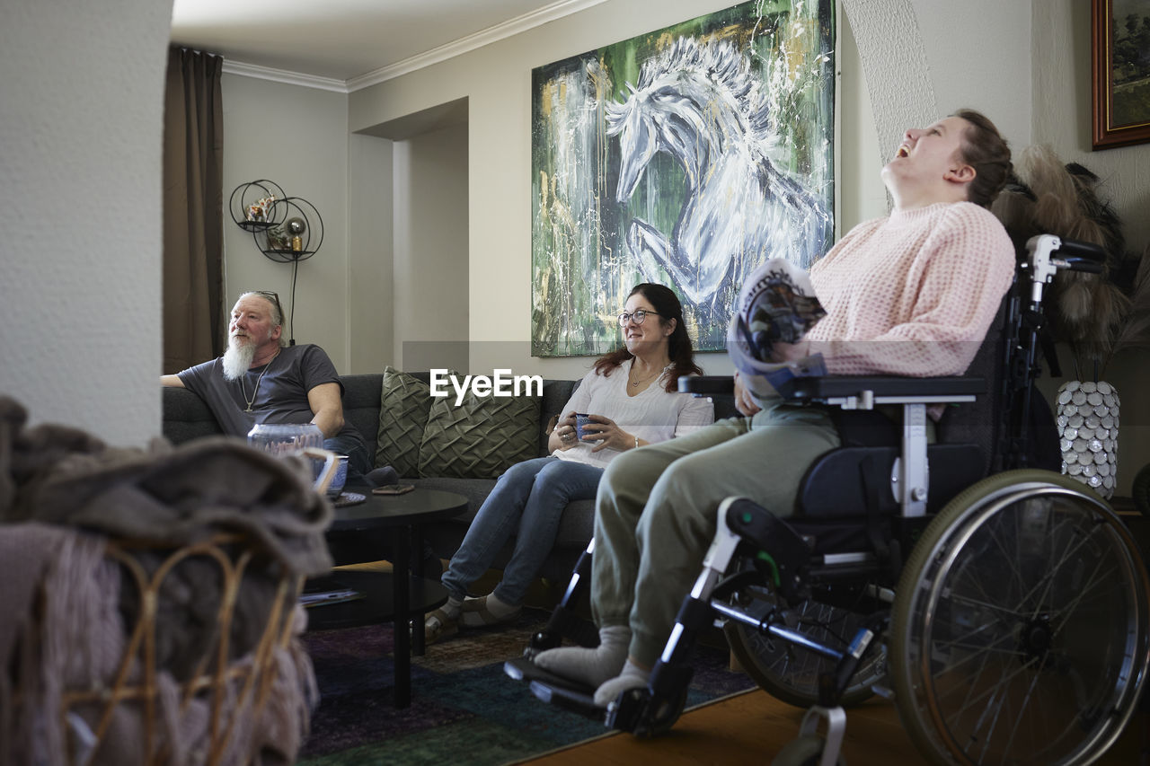 Parents with disabled daughter in wheelchair relaxing in living room