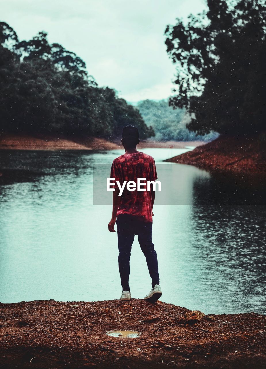 Rear view of man standing by lake against sky