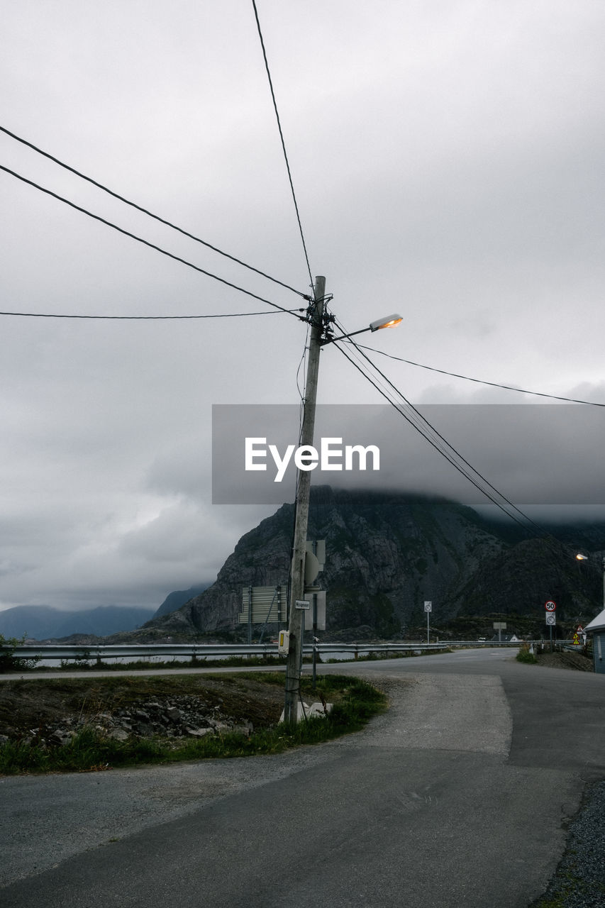 Electricity pylon by road against mountains and sky