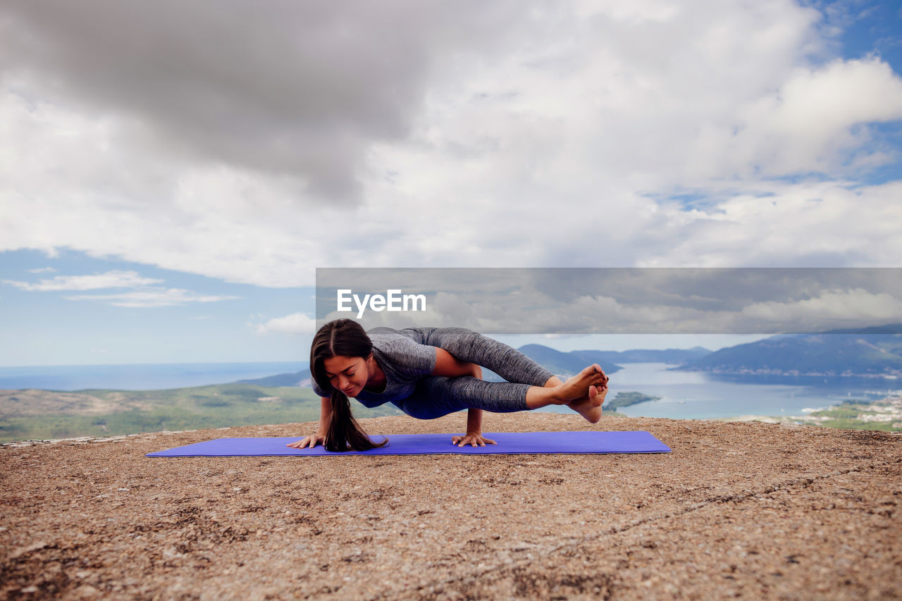 Woman exercising on mountain against cloudy sky