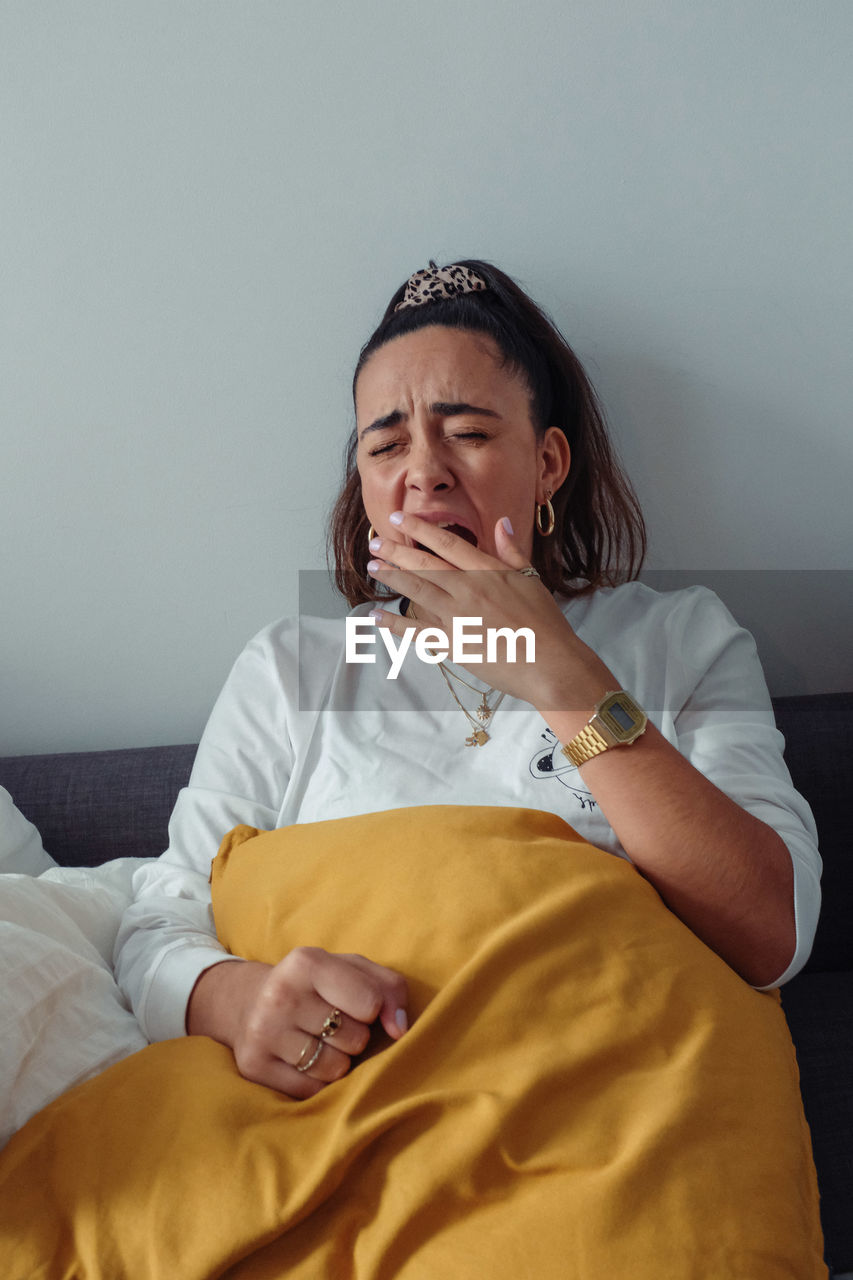 Young woman yawning while sitting on bed at home