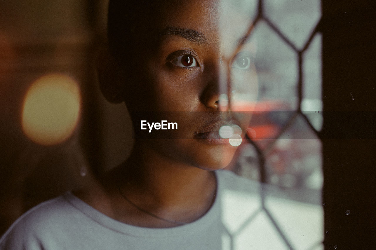 CLOSE-UP PORTRAIT OF YOUNG MAN LOOKING THROUGH WINDOW