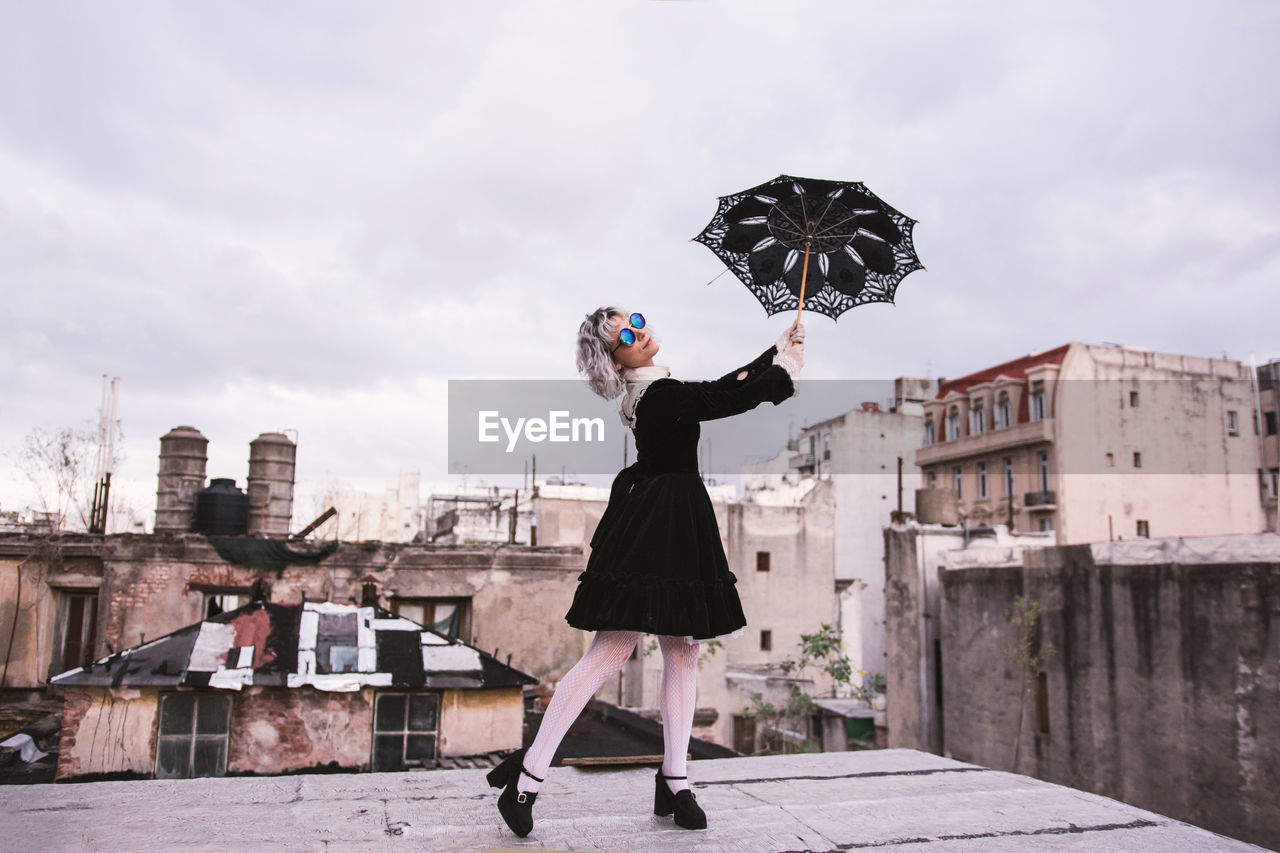 Low angle view of woman holding umbrella on terrace against sky