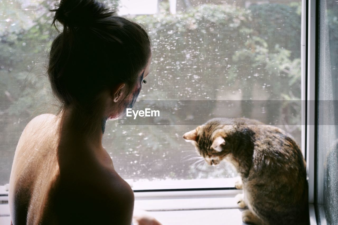 Shirtless woman with cat at window sill