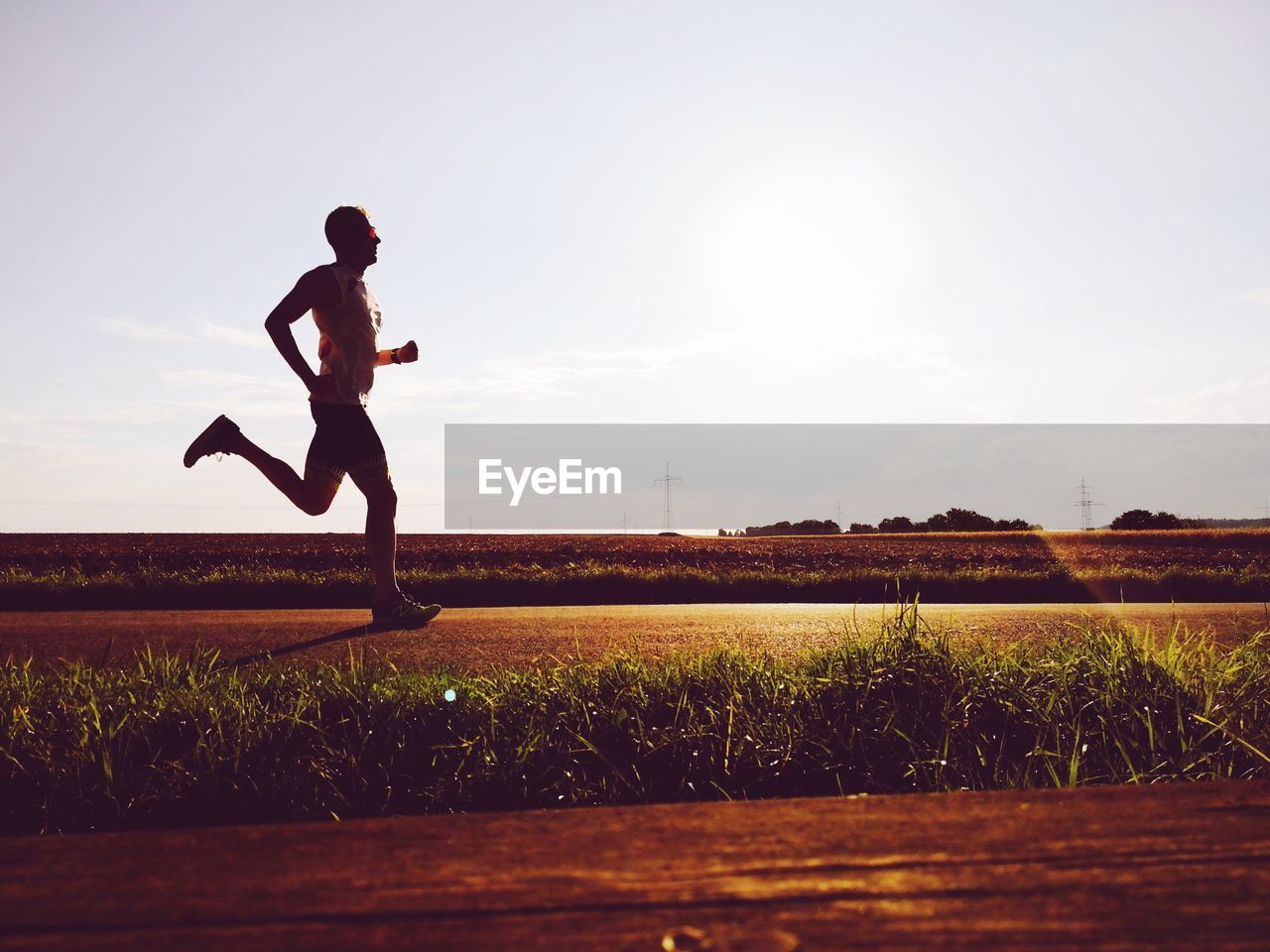 Side view of man running on field against sky during sunny day