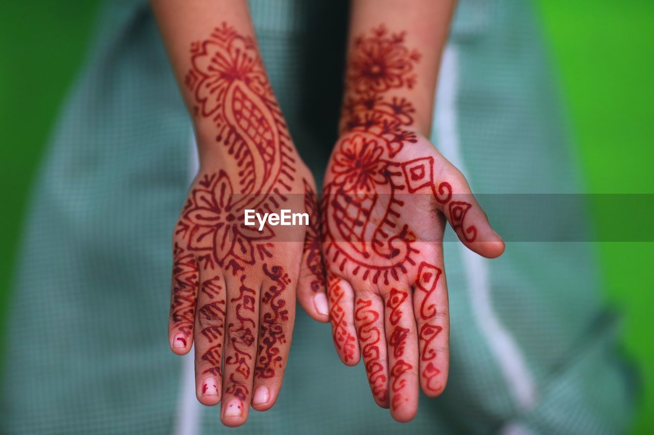 Cropped image of person showing henna tattooed hand