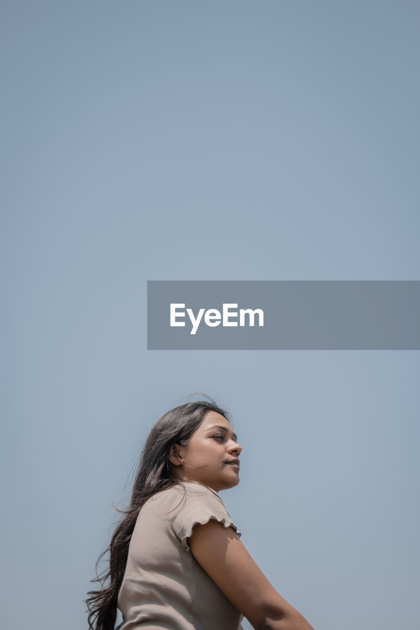 Young woman looking away against clear sky