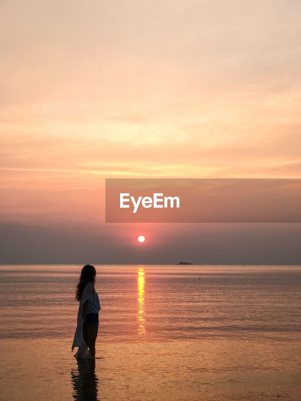 Side view of woman standing on shore against sky during sunset