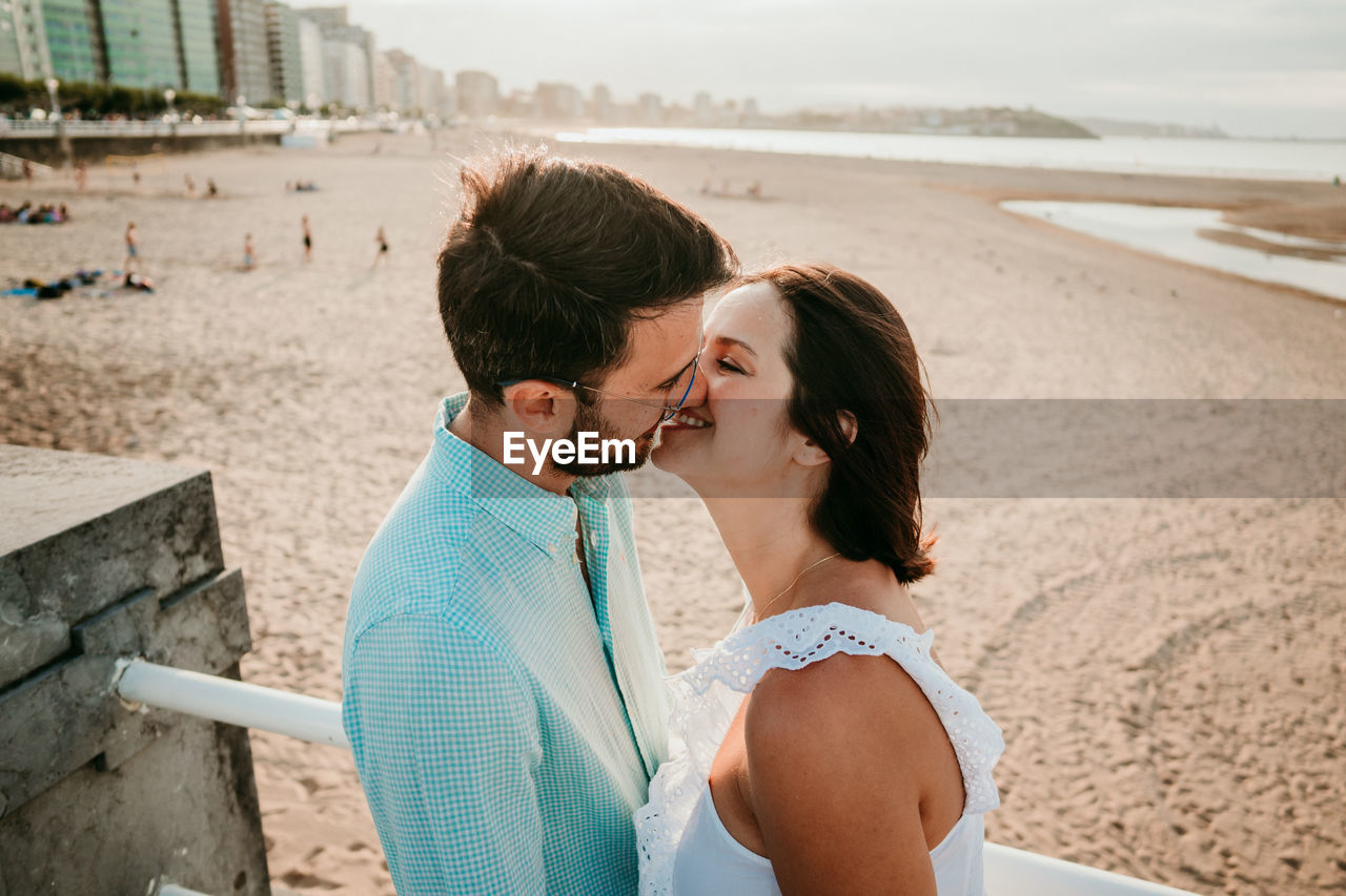 Full length of couple embracing while standing on beach against sky