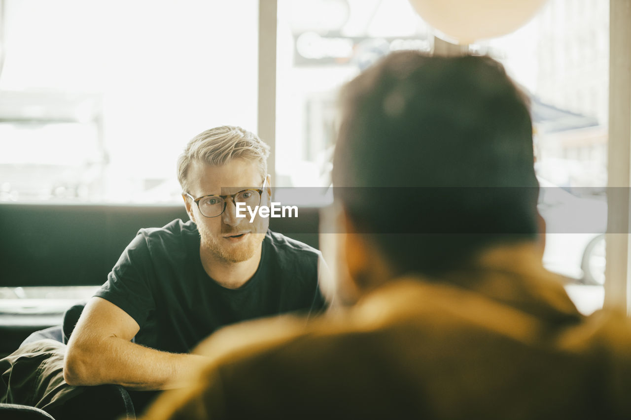 Mid adult man talking to friend while sitting in restaurant