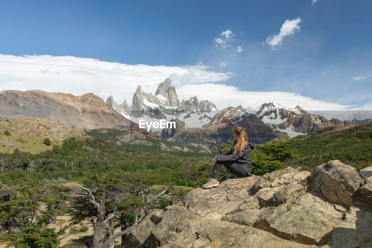 rear view of man sitting on mountain against sky