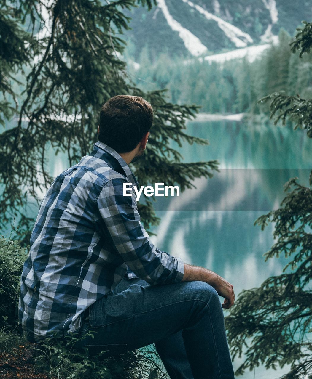 Side view of young man looking at lake with mountain reflection