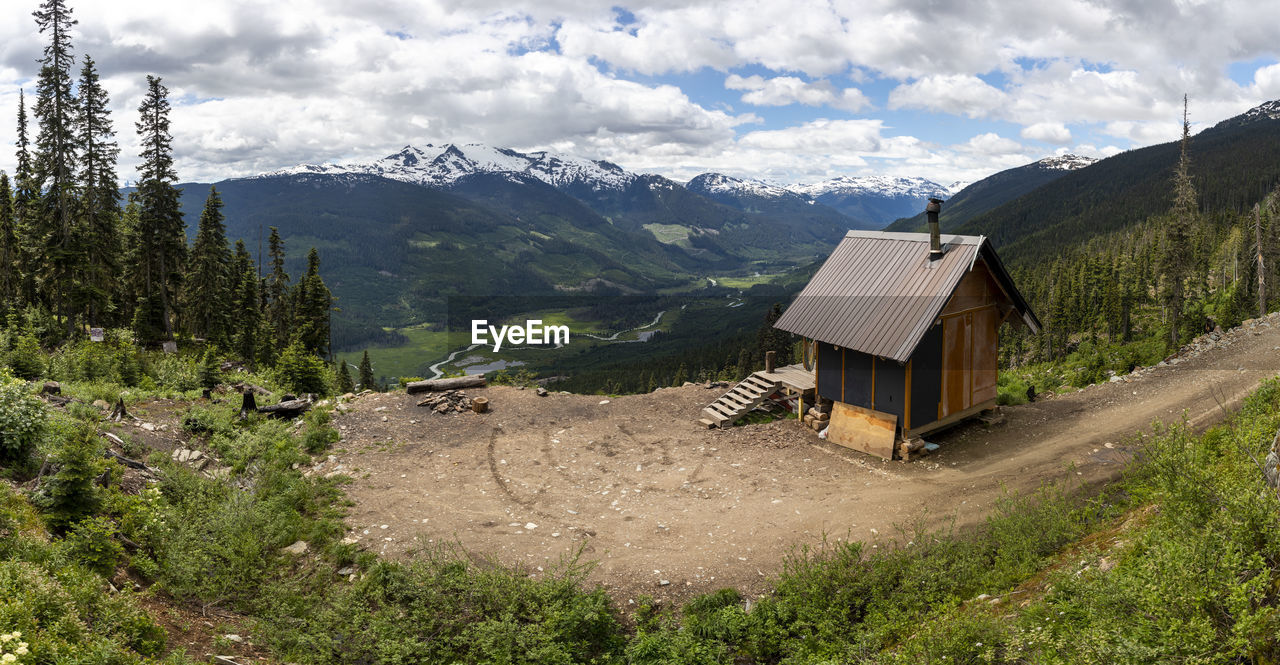 Small cabin located near logging road against snowy mountains and cloudy sky in highlands of british columbia, canada