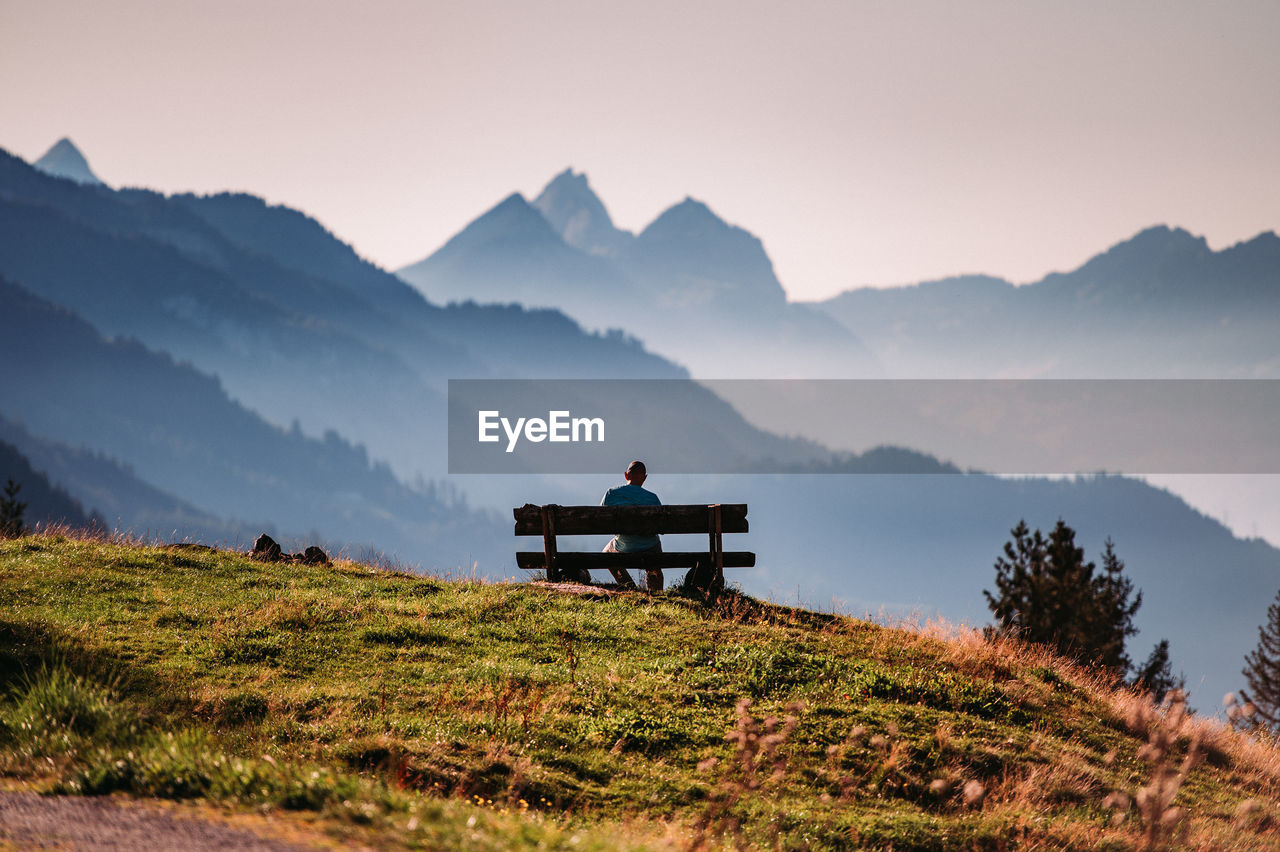 Man sitting on bench against mountain range