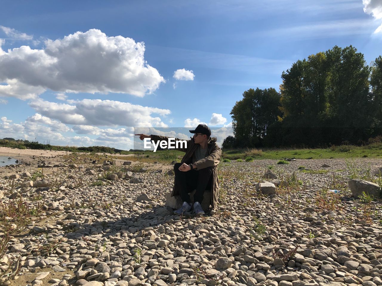 Young man pointing while sitting at beach