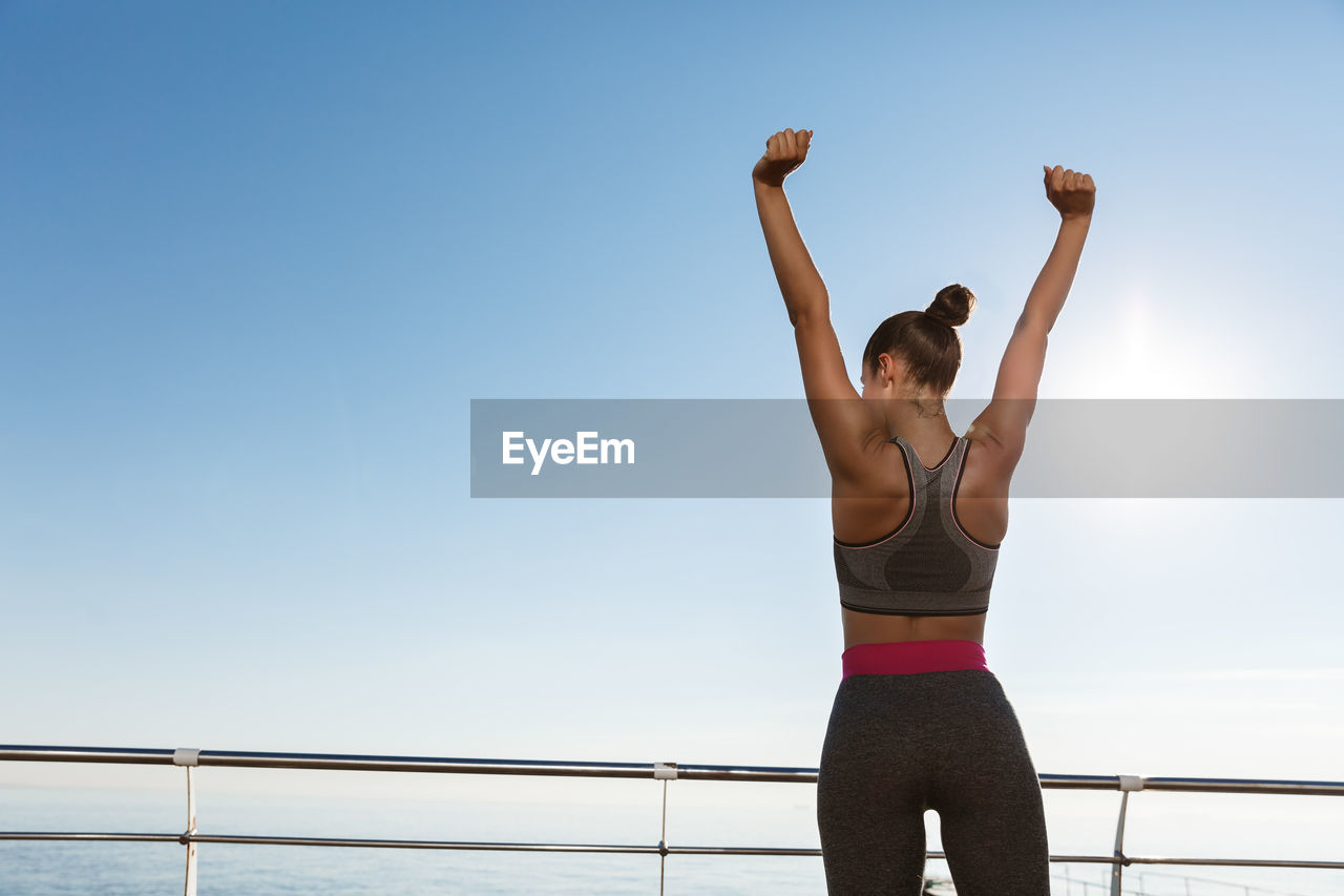 Woman exercising while standing against sea and sky