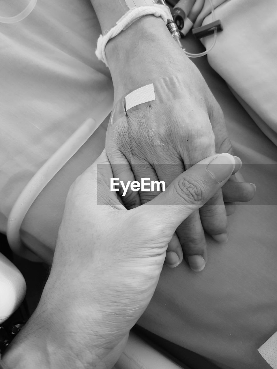 Cropped image of man holding hands with female patient on hospital bed