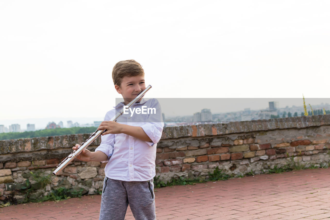 Boy playing flute against clear sky