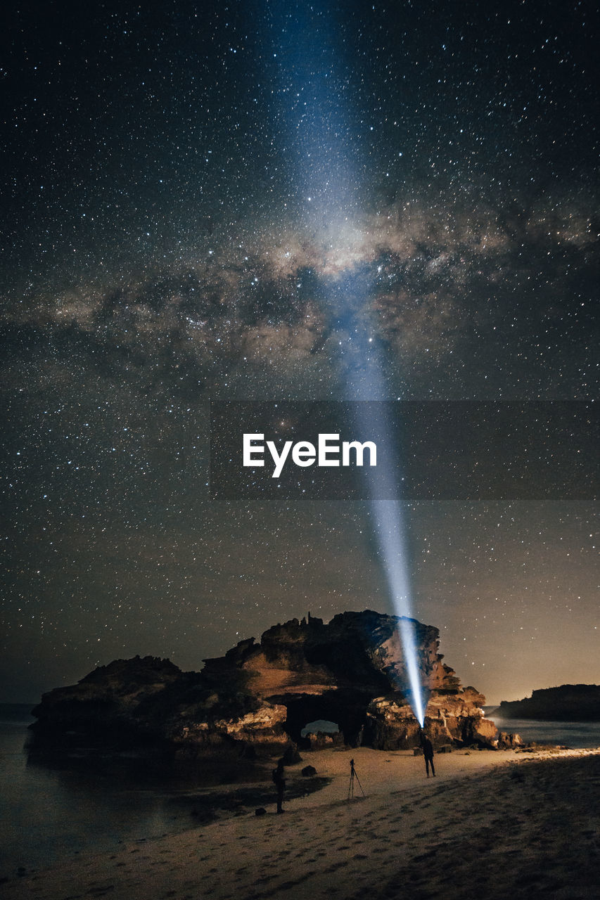 Man pointing flashlight towards stars in sky