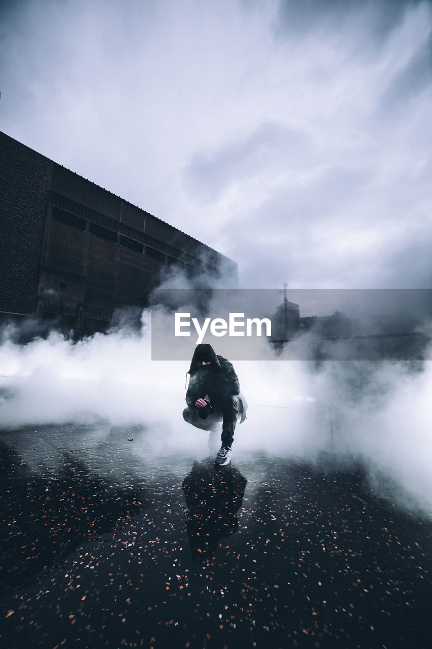 Man wearing hoodie standing amidst smoke on street