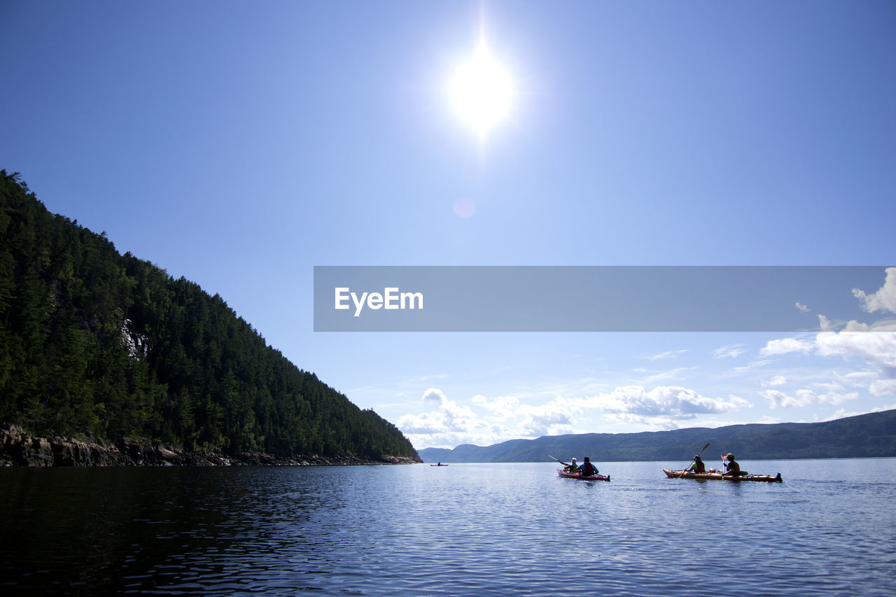 People boating on sea against sky during sunny day