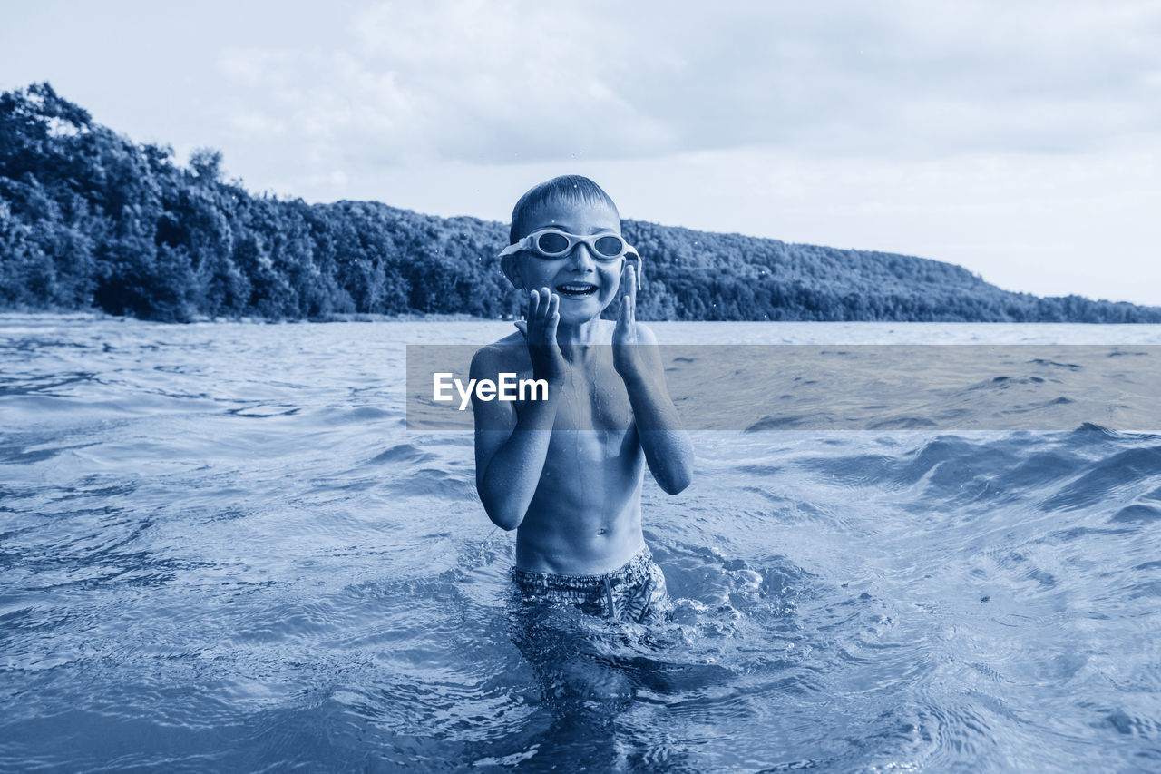 Portrait of shirtless boy in lake against sky