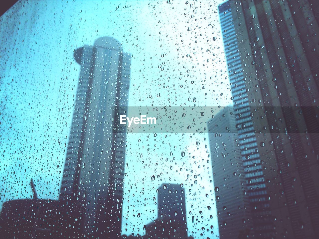 Low angle view of skyscrapers seen through wet glass window