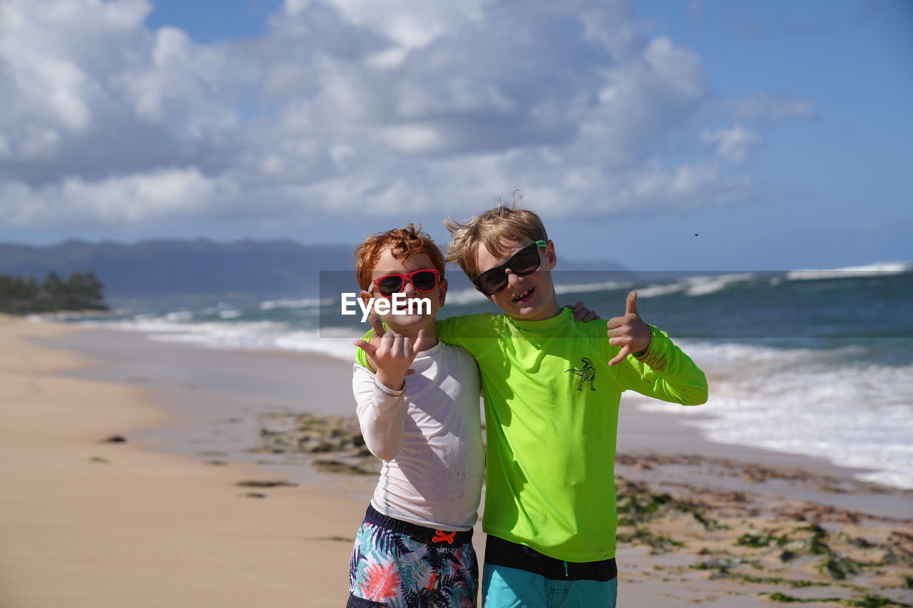 Young boy smiling with an aloha sign wearing sunglasses on the beach in hawaii. 