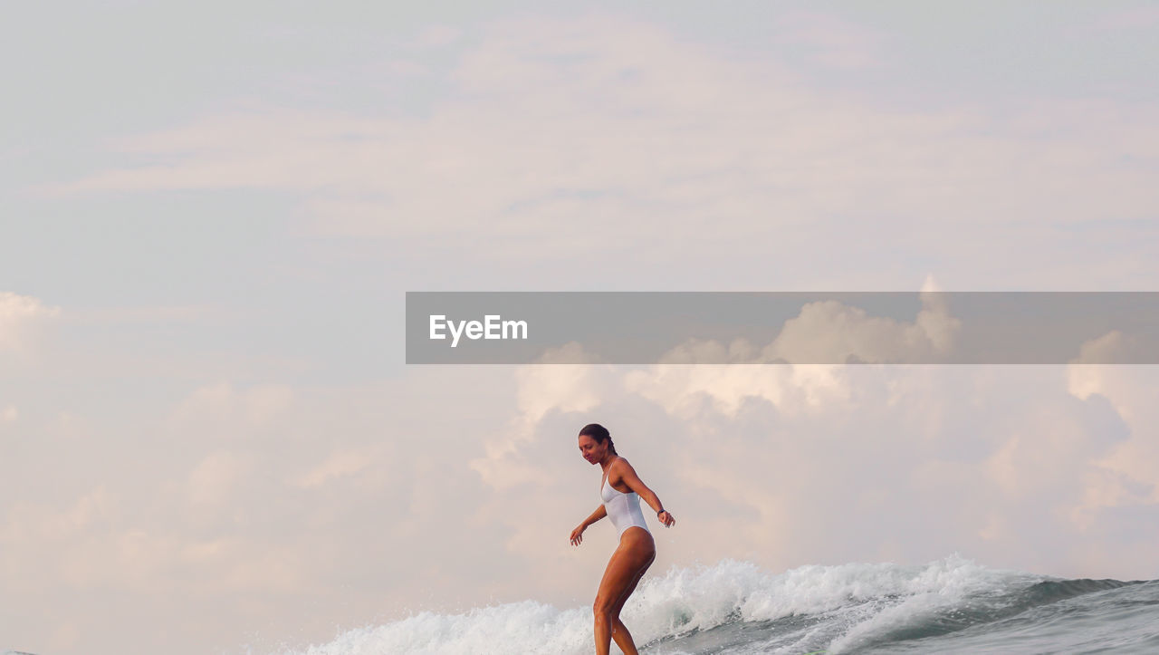 Side view of young woman surfing on sea against sky