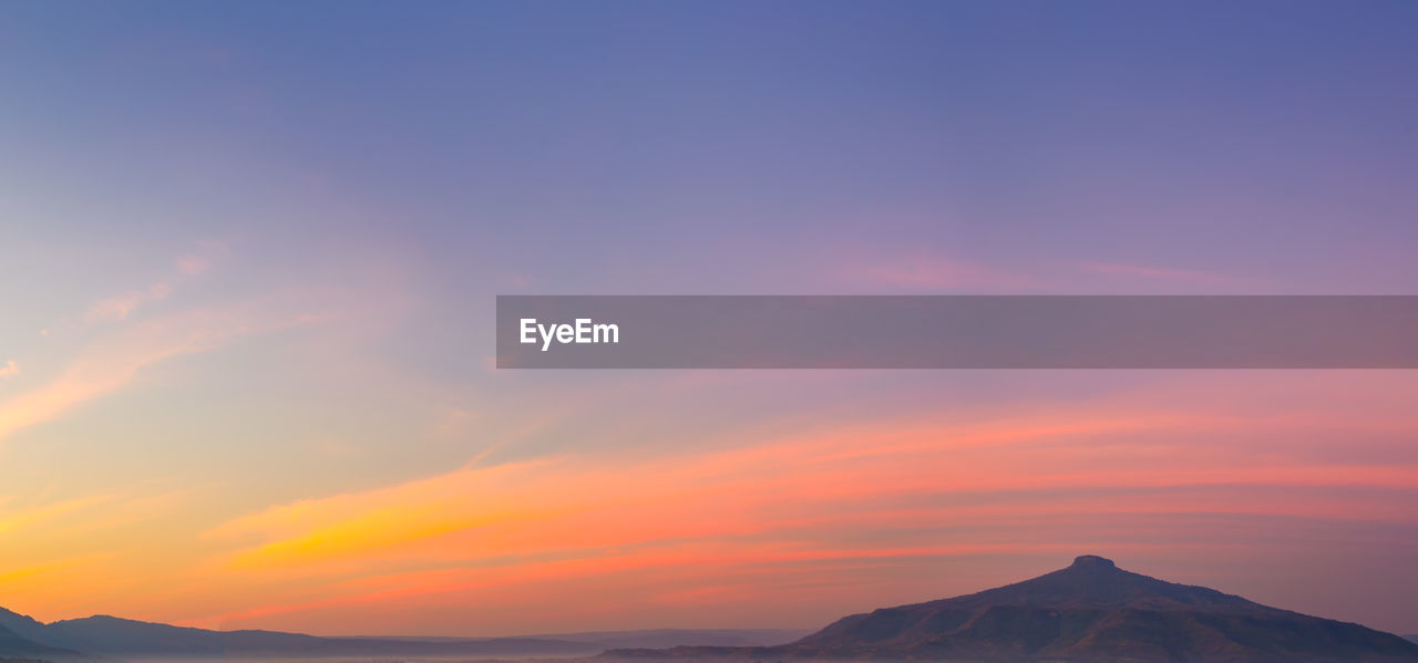 LOW ANGLE VIEW OF SILHOUETTE MOUNTAIN AGAINST DRAMATIC SKY DURING SUNSET