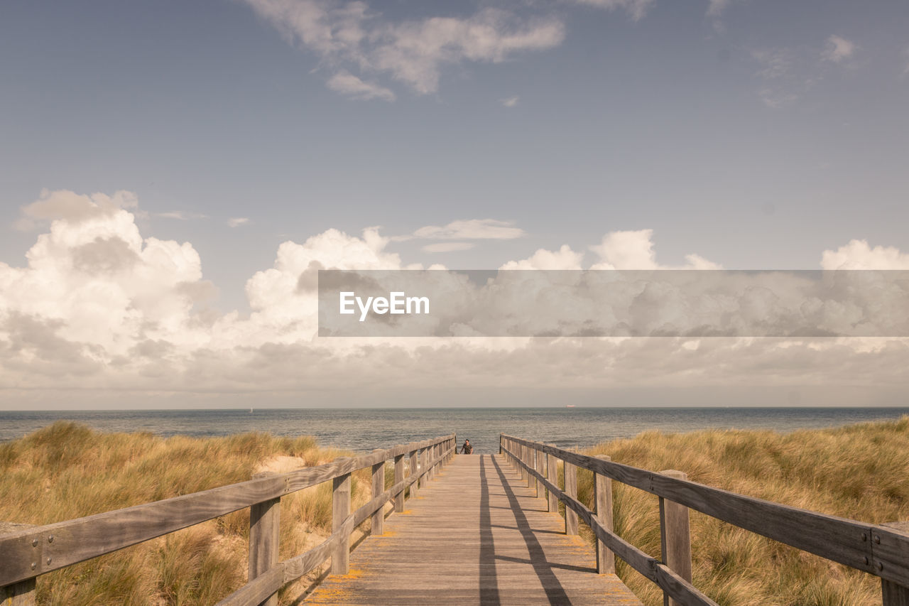Scenic view of pier, sea and dunes against sky
