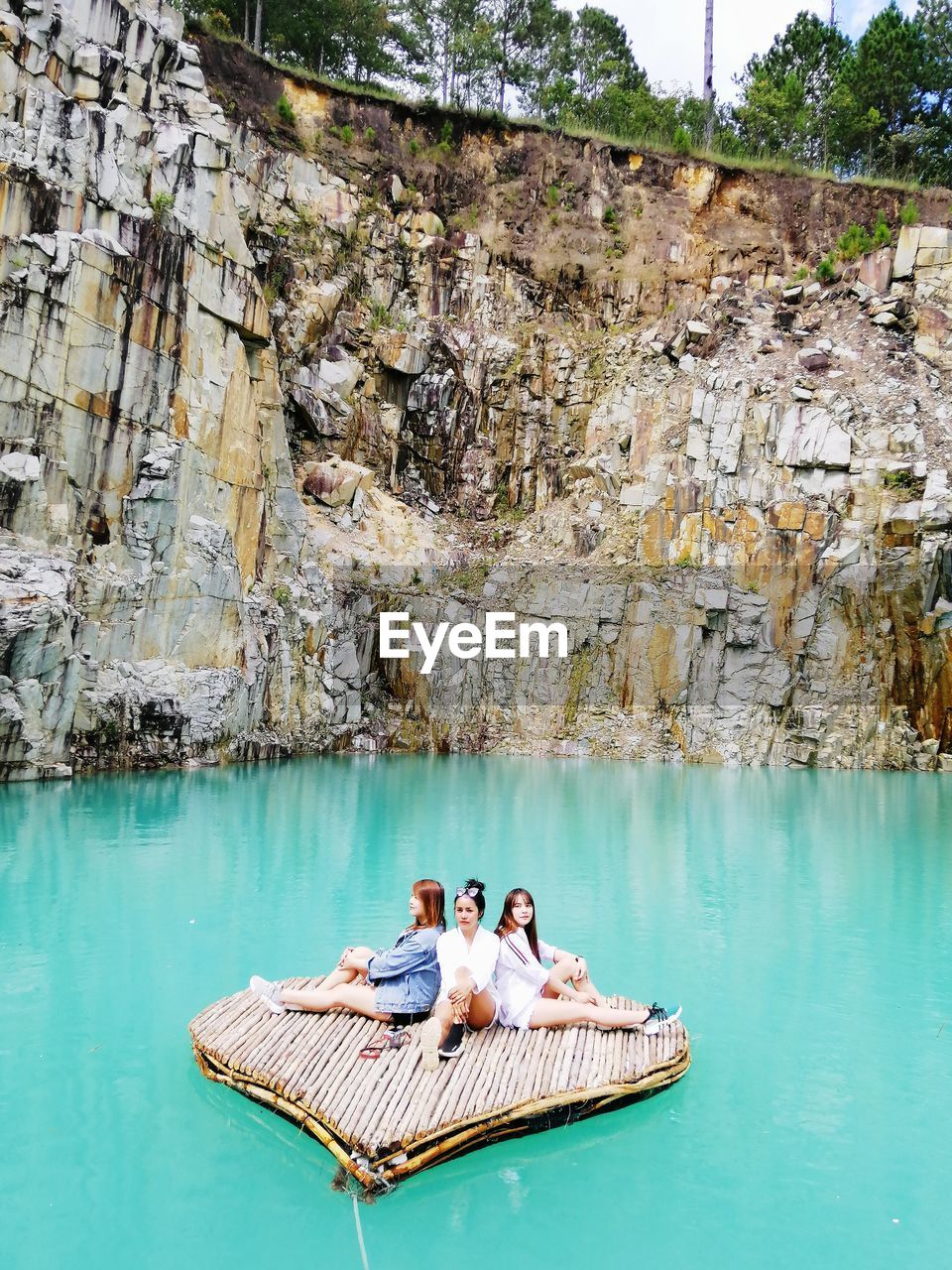 Friends sitting on raft amidst lake against cliff