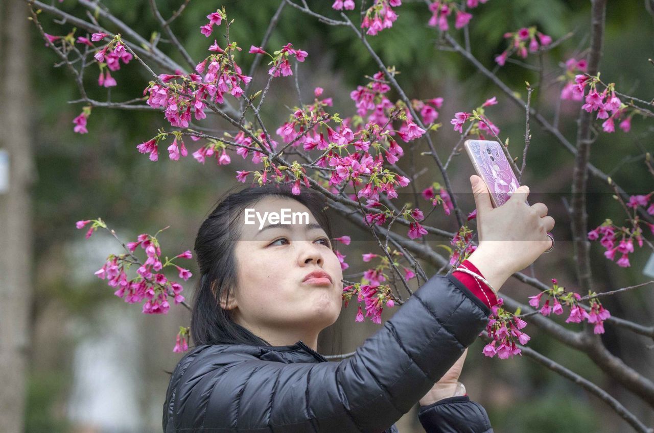 YOUNG WOMAN WITH FLOWERS BLOOMING IN PARK